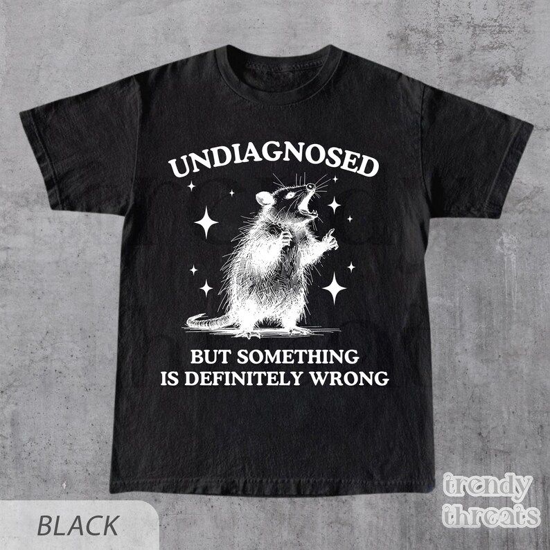 May include: Black t-shirt with a distressed graphic of a rat and the text "UNDIAGNOSED BUT SOMETHING IS DEFINITELY WRONG." The shirt also has a "trendy threats" logo in the bottom right corner.