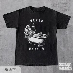 May include: Black t-shirt with a white skeleton in a bathtub holding a cup of coffee. The text "Never Better" is printed below the skeleton.