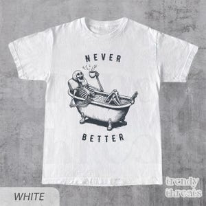 May include: White t-shirt with a black and white illustration of a skeleton in a bathtub. The skeleton is holding a cup and the text "NEVER BETTER" is printed below the image.