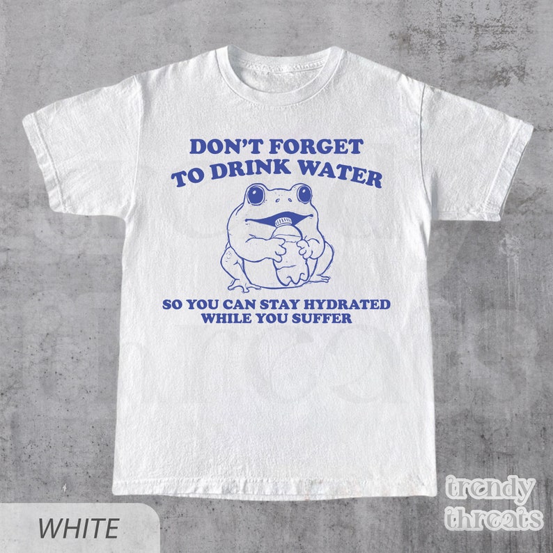 K&ouml;nnte beinhalten: Wei&szlig;es T-Shirt mit einem blauen Comic-Frosch, der eine Wasserflasche h&auml;lt. Der Text auf dem Shirt lautet "Vergiss nicht, Wasser zu trinken, damit du hydriert bleibst, w&auml;hrend du leidest."