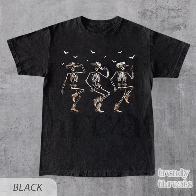 May include: Black t-shirt with a graphic of three skeletons wearing cowboy hats and boots, dancing. The skeletons are outlined in white and have a vintage look. Bats are flying above the skeletons.