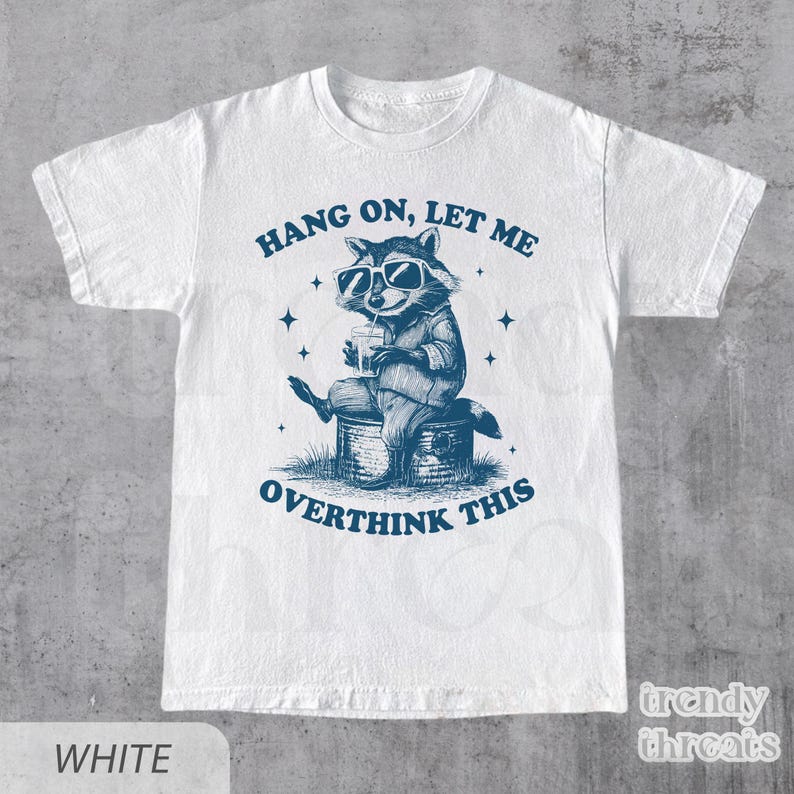 May include: White t-shirt with a blue graphic of a raccoon wearing sunglasses and holding a drink. The text "Hang on, let me overthink this" is printed on the shirt.