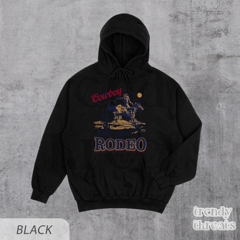 May include: Black hooded sweatshirt with a graphic print of a cowboy riding a horse with the text "Cowboy Rodeo" in red and blue.
