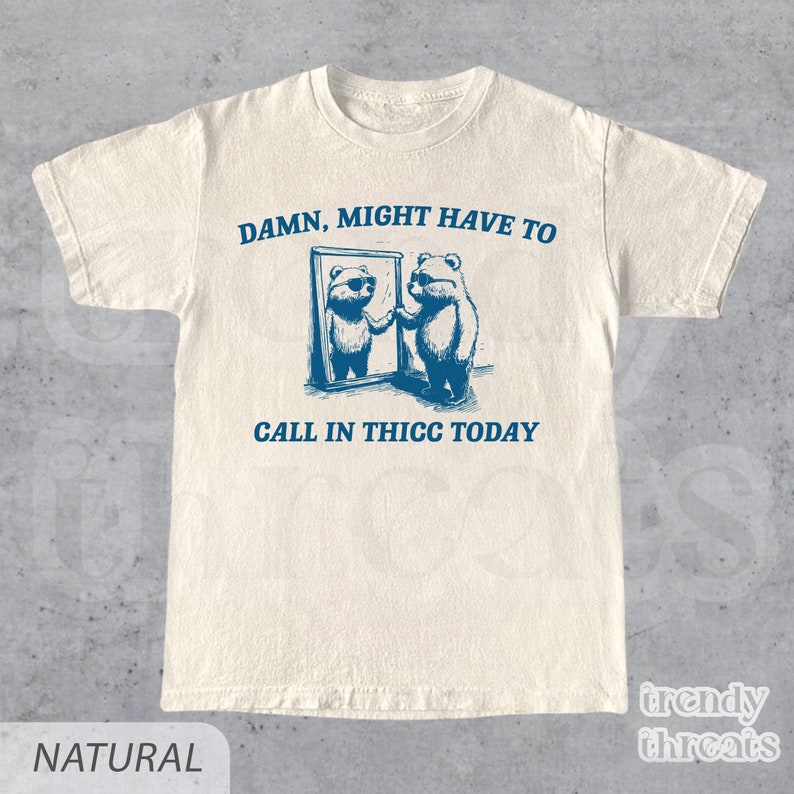 May include: A white t-shirt with a blue graphic of two bears looking in a mirror. The text "DAMN, MIGHT HAVE TO CALL IN THICC TODAY" is printed on the shirt.