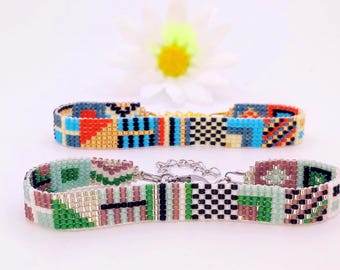 May include: Two beaded bracelets with colourful geometric patterns. The top bracelet features blue, red, and gold beads, while the bottom one has green, pink, and black beads. Both have chain fastenings.