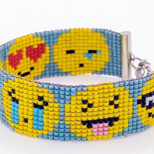 Könnte beinhalten: Ein Armband mit Perlen, das verschiedene Emoji-Gesichter in Gelb, Schwarz, Rot und Blau zeigt. Das Armband hat einen hellblauen Rand und einen silbernen Verschluss. Die Emojis zeigen ein Herzaugen-, weinendes und herausgestrecktes Zungen-Gesicht.