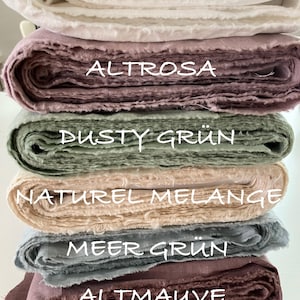 May include: A stack of six folded fabric bolts in various colors. The labels on the fabric read ECRU, ALTROSA, DUSTY GR&Uuml;N, NATUREL MELANGE, MEER GR&Uuml;N, and ALTMAUVE. Each bolt features a textured, woven appearance with raw, frayed edges visible.