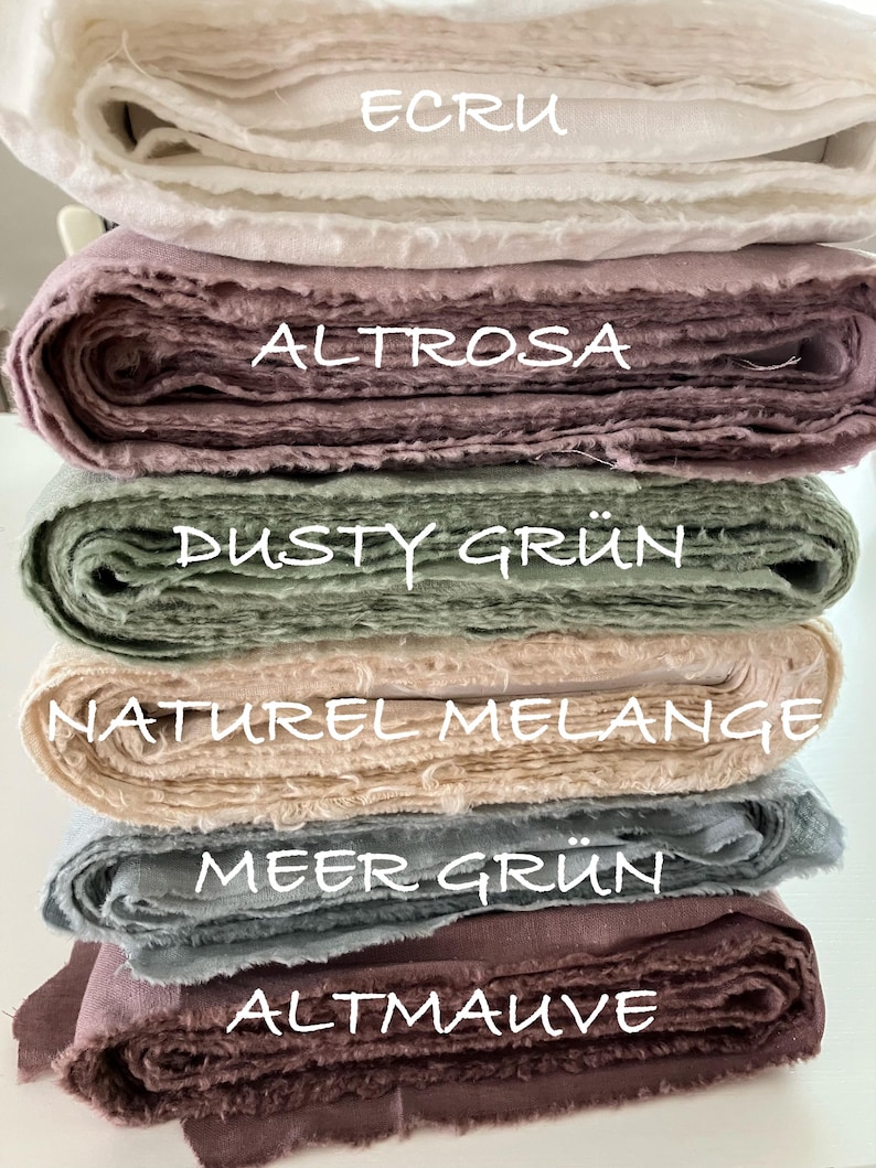 May include: A stack of six folded fabric bolts in various colors. The labels on the fabric read ECRU, ALTROSA, DUSTY GR&Uuml;N, NATUREL MELANGE, MEER GR&Uuml;N, and ALTMAUVE. Each bolt features a textured, woven appearance with raw, frayed edges visible.