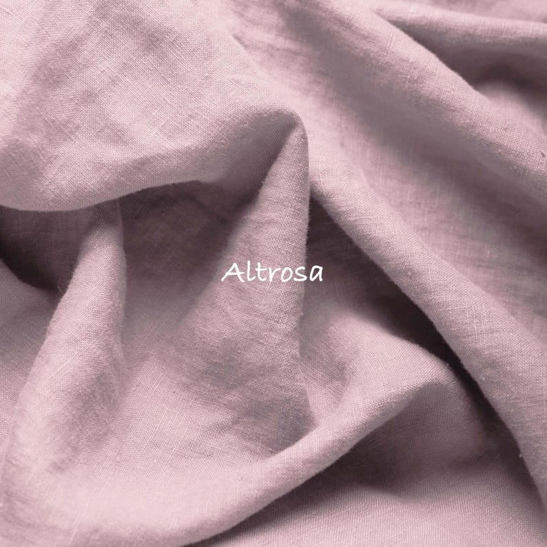 May include: A piece of dusty rose colored fabric with a visible woven texture and folds. The word Altrosa is printed in white text on the surface of the fabric. The material has a matte finish and shows natural creases throughout the textile.
