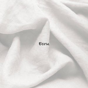 May include: A piece of white fabric with a visible woven texture and soft folds. The word Ecru is printed in black, sans-serif lettering in the center of the fabric. The material appears lightweight and has a matte finish throughout the surface.