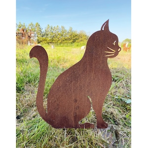 May include: A rusty metal silhouette of a cat sitting in a grassy field. The cat is facing to the right and has a long tail.