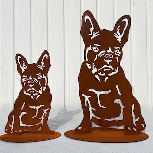 Könnte beinhalten: Zwei Metallskulpturen von französischen Bulldoggen, eine große und eine kleine, beide in sitzender Position. Die Skulpturen sind aus rostigem Metall und haben eine braune Farbe.
