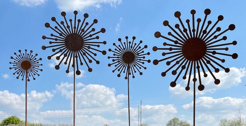 May include: Four metal sculptures of stylised dandelions with a rusty brown colour against a blue sky with white clouds.