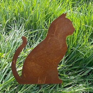 Könnte beinhalten: Eine rostige Metallsilhouette einer Katze, die in einem grasbewachsenen Bereich sitzt. Die Katze blickt nach rechts und hat einen langen Schwanz.