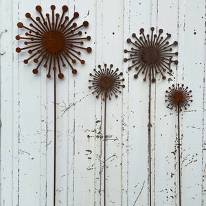May include: Four rusty metal dandelion sculptures with long stems against a white painted wood background.