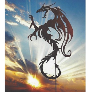 Könnte beinhalten: Eine schwarze Metallsilhouette eines Drachen mit filigranen Details, in stehender Position mit ausgebreiteten Flügeln. Der Drache ist vor dem Hintergrund eines bewölkten Himmels mit einer strahlenden Sonne, die durch die Wolken scheint, platziert.