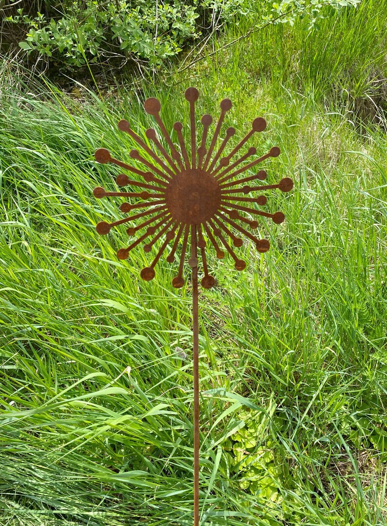 May include: A rusty metal garden stake shaped like a dandelion with a round centre and many thin, pointed petals.