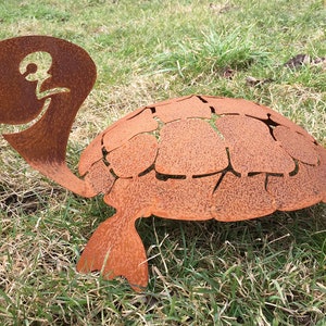 Könnte beinhalten: Eine rostige Metallschildkrötenskulptur mit einem Ausschnittmuster. Die Schildkröte steht auf einem Bett aus grünem Gras.