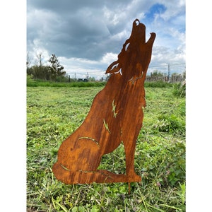 May include: A rusty metal silhouette of a wolf howling at the moon. The wolf is sitting on a bed of green grass.