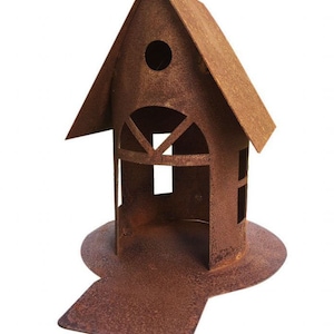 Könnte beinhalten: Ein rostiges Vogelhaus aus Metall mit einem spitzen Dach und einer kleinen Öffnung, durch die Vögel eintreten können. Das Vogelhaus steht auf einem Metallpfahl und hat eine kleine Plattform, auf der Vögel landen können.