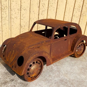 Pode incluir: Uma escultura de metal enferrujado de um carro clássico, que se assemelha a um Volkswagen Beetle. O carro é detalhado com uma carroceria arredondada, um pára-brisas e rodas. A escultura é uma peça única e decorativa.
