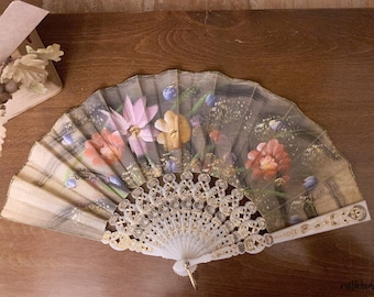 May include: A white folding fan with a gold trim and a floral design. The fan features painted flowers in shades of pink, red, yellow, and blue.