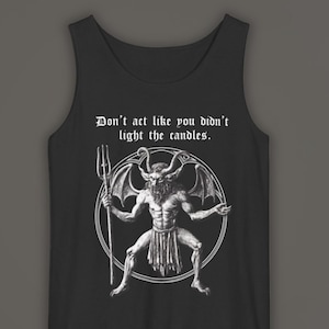 May include: A black tank top featuring a white graphic print of a horned, winged figure holding a trident inside a circle. Above the graphic, the text reads: Don't act like you didn't light the candles. The garment has a scoop neckline and sleeveless design.