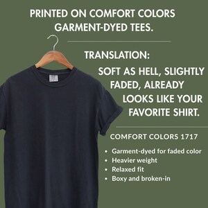 May include: A black short-sleeved t-shirt on a wooden hanger. Text reads: PRINTED ON COMFORT COLORS GARMENT-DYED TEES. TRANSLATION: SOFT AS HELL, SLIGHTLY FADED, ALREADY LOOKS LIKE YOUR FAVORITE SHIRT. COMFORT COLORS 1717. Garment-dyed, heavier weight, relaxed fit.