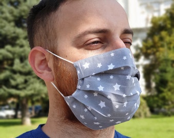 May include: A man wearing a gray face mask with white stars. The mask is pleated and has a white elastic band.