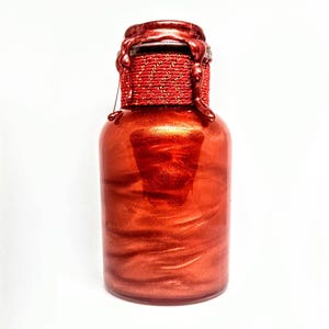 May include: A red glass bottle with a gold metallic finish and a red wax seal around the top.