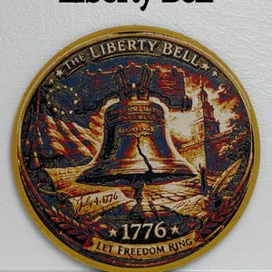 May include: A round, gold-edged emblem featuring the Liberty Bell, an American flag, and Independence Hall. The text "Liberty Bell" is at the top, with "July 4, 1776" and "1776 LET FREEDOM RING" at the bottom. The image is a patriotic design.
