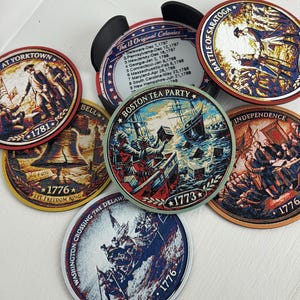 May include: A collection of round coasters featuring historical American Revolution scenes and text. The coasters depict events like the Boston Tea Party, the Battle of Saratoga, and the signing of the Declaration of Independence. Each coaster has a different illustration and the year 1776 or 1773.