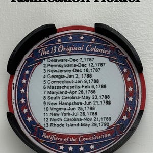 May include: A black and red Ratification Holder with the text "Ratification Holder" at the top. The holder features a circular design with the text "The 13 Original Colonies" and a list of dates.