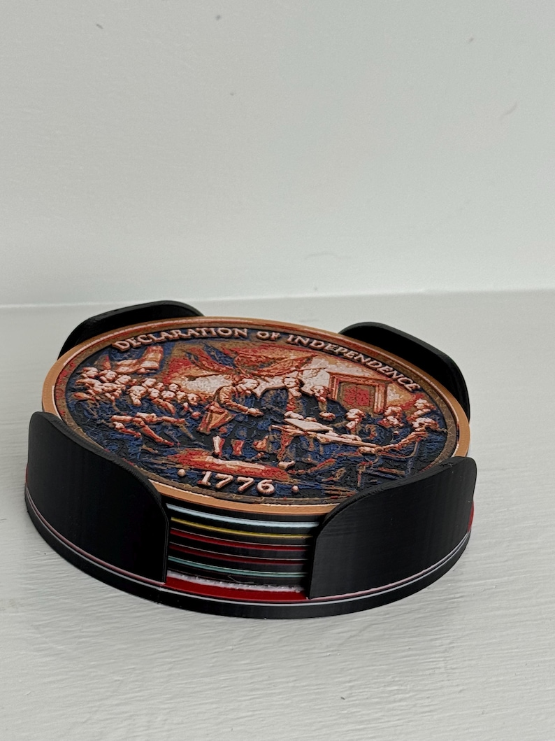 May include: A set of coasters featuring a depiction of the signing of the Declaration of Independence, with the text "DECLARATION OF INDEPENDENCE" and "1776". The coasters are held in a black holder.