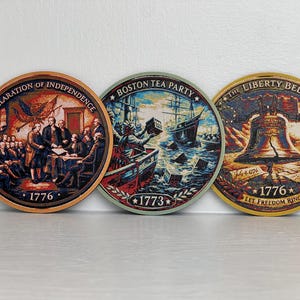 May include: Three round coasters with historical American scenes. One depicts the Declaration of Independence, another the Boston Tea Party, and the third the Liberty Bell. Each coaster has the year 1776 or 1773.