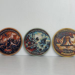 May include: Three round decorative items featuring historical scenes. One depicts the Declaration of Independence, another the Boston Tea Party, and the third the Liberty Bell. Each item has the year 1776 or 1773 printed on it.