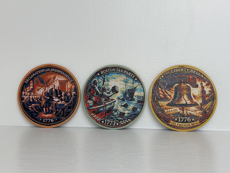 May include: Three round decorative items featuring historical scenes. One depicts the Declaration of Independence, another the Boston Tea Party, and the third the Liberty Bell. Each item has the year 1776 or 1773 printed on it.