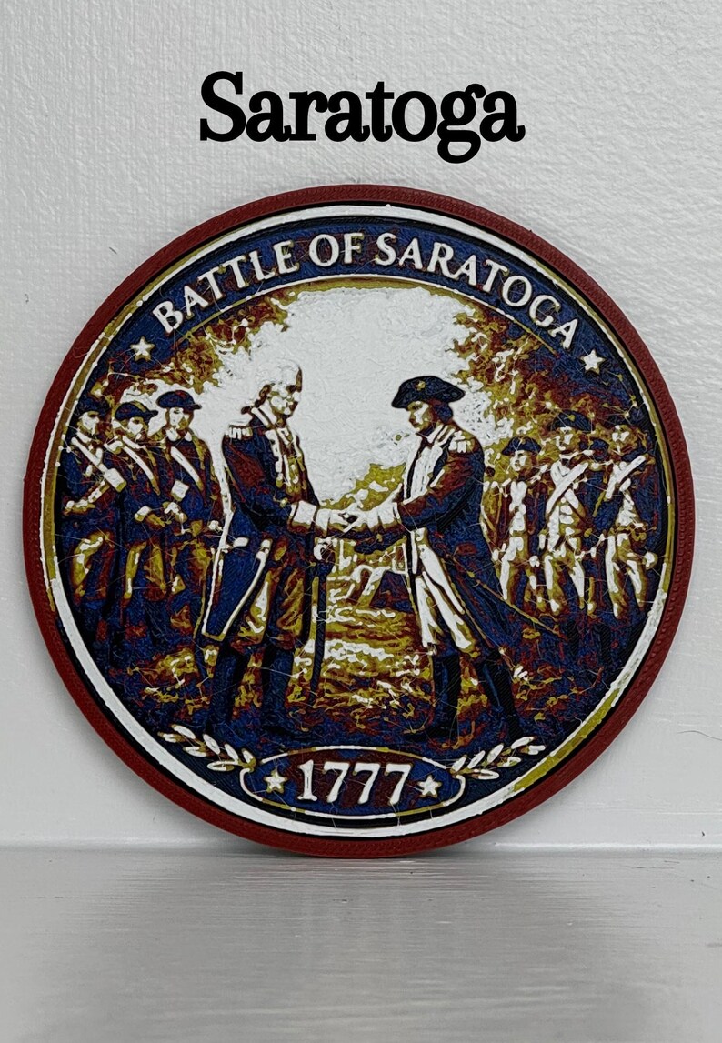 May include: Circular emblem with the text "Saratoga" at the top. The emblem features an illustration of two men shaking hands, surrounded by other figures. The words "BATTLE OF SARATOGA" and the year "1777" are also present.
