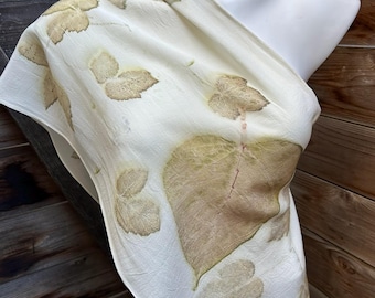 May include: A white silk scarf with a leaf pattern in shades of brown and green. The scarf is draped over a white mannequin.