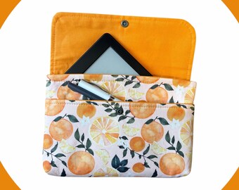 May include: An orange and white patterned e-reader case with a flap. The case features a design of oranges and leaves. Inside, a black e-reader and a pen are visible. The interior is a solid orange color.