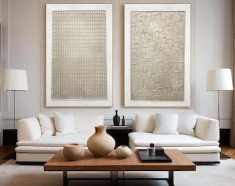 Puede incluir: Dos grandes pinturas abstractas en marcos blancos, una con un patrón geométrico y la otra con un diseño texturizado, cuelgan sobre un sofá seccional blanco con una mesa de café de madera y jarrones decorativos.