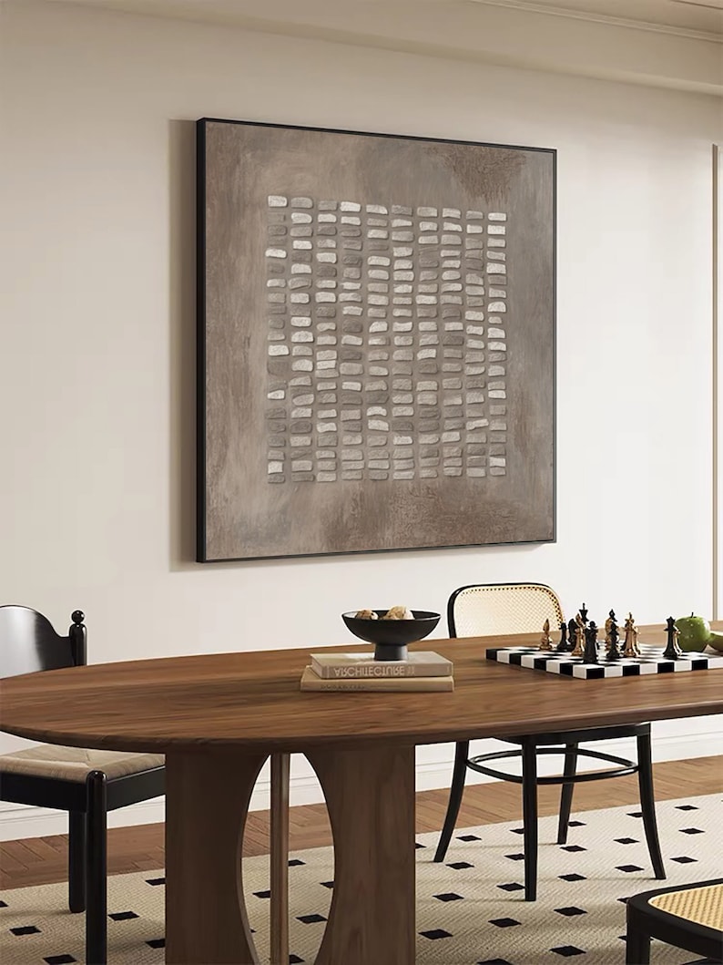 May include: A brown and white abstract painting with a geometric pattern hangs on a white wall above a wooden dining table with black chairs. A chessboard with black and white pieces sits on the table.