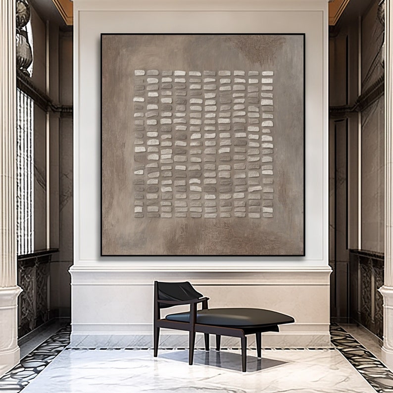 May include: Abstract painting with a geometric pattern of white and gray rectangles on a brown background. The painting is hanging on a wall in a room with a black chair.