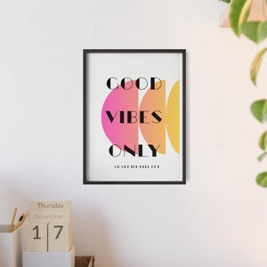 Könnte beinhalten: Ein gerahmter Kunstdruck mit den Worten "GOOD VIBES ONLY" in schwarzer Schrift, mit einem rosa, orangefarbenen und gelben geometrischen Design. Der Druck ist in einem schwarzen Rahmen und hängt an einer weißen Wand.