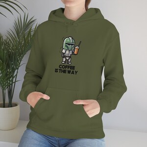 Puede incluir: Una sudadera con capucha verde con una imagen de dibujos animados de un personaje de Star Wars sosteniendo una taza de caf&eacute;. El texto "COFFEE IS THE WAY" est&aacute; impreso debajo de la imagen.