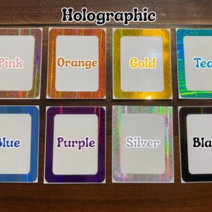 K&ouml;nnte beinhalten: Acht holografische Aufkleber in verschiedenen Farben, darunter Rosa, Orange, Gold, T&uuml;rkis, Blau, Lila, Silber und Schwarz. Jeder Aufkleber hat eine rechteckige Form mit einem wei&szlig;en Zentrum und einem farbigen Rand. Das Wort "Holographic" steht oben.