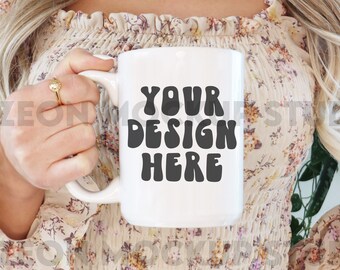 May include: A white ceramic mug with a black design that says "YOUR DESIGN HERE" in a retro font. The mug is being held by a person wearing a floral blouse and blue jeans.