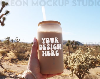 May include: A clear reusable glass tumbler with a bamboo lid and a straw. The tumbler is filled with a brown liquid and has the text "YOUR DESIGN HERE" in white letters.