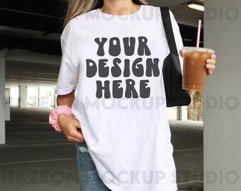 May include: A white oversized t-shirt with the text "YOUR DESIGN HERE" in black. The shirt is being worn by a person in a casual setting.