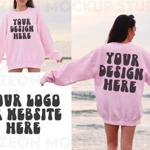 May include: A pink sweatshirt with the text "YOUR DESIGN HERE" in black on the front and the text "YOUR LOGO OR WEBSITE HERE" in black on the back. The sweatshirt is being worn by a person standing on a beach.